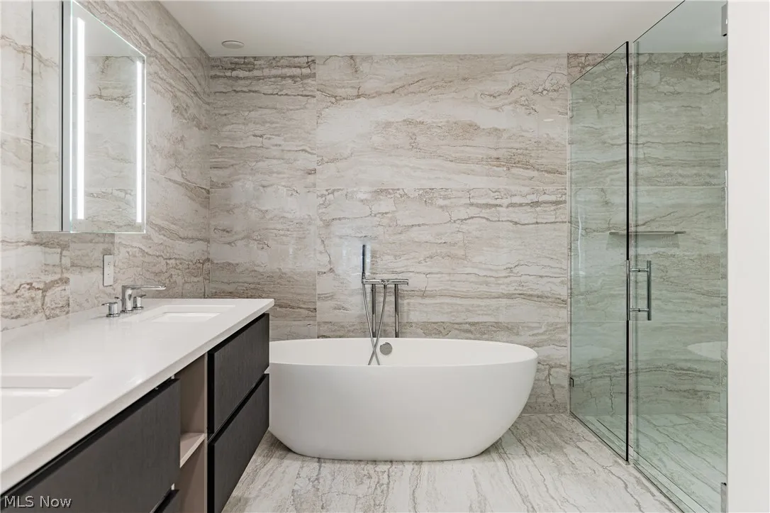 Bathroom with independent shower and bath, tile floors, tile walls, and double sink vanity
