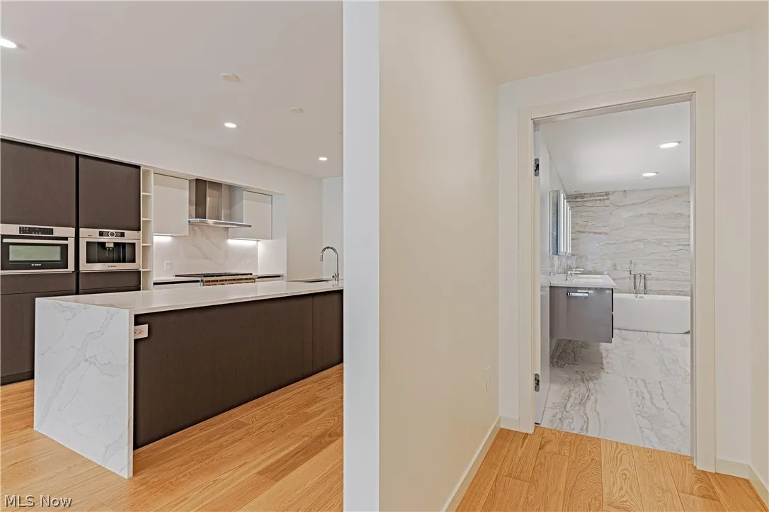 Kitchen with a center island, wall chimney range hood, dark brown cabinets, sink, and light tile floors