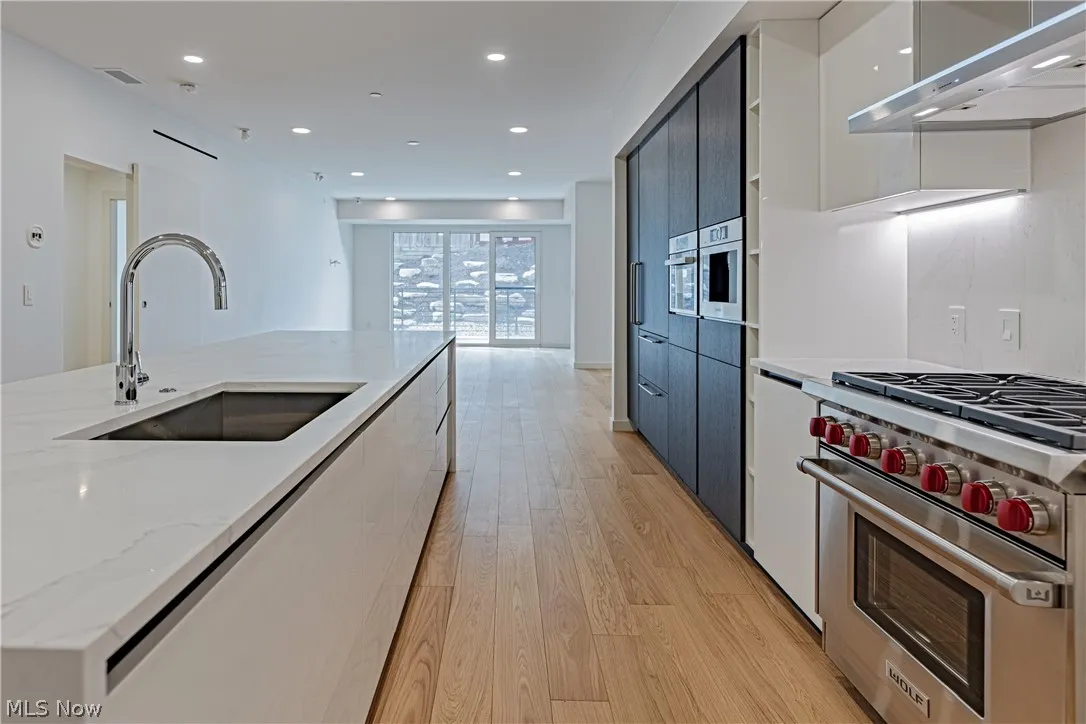Kitchen featuring wall chimney exhaust hood, light wood-type flooring, sink, light stone counters, and premium range