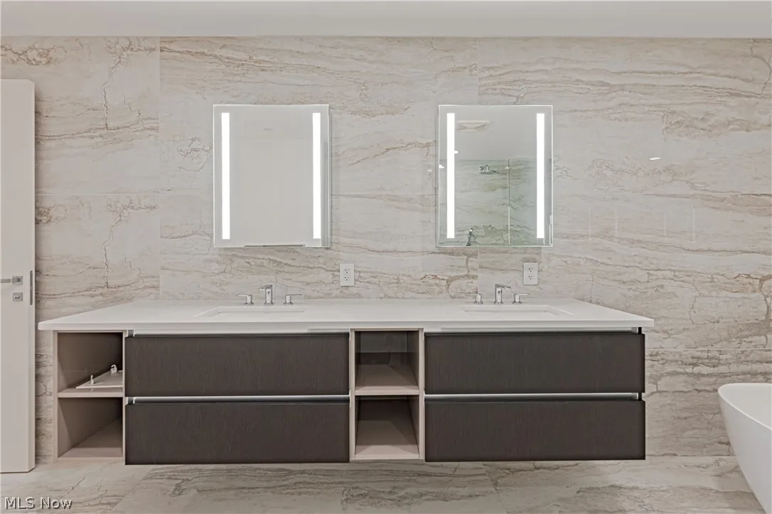Bathroom featuring tile walls, a bathtub, tile floors, and double sink vanity