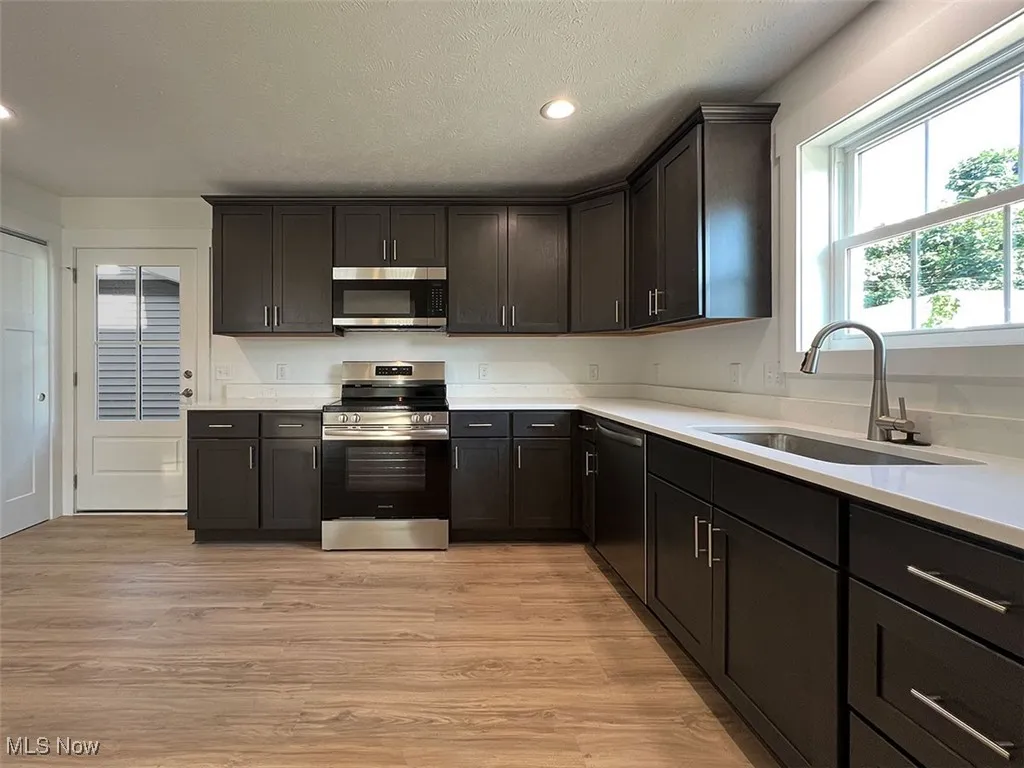 Kitchen with appliances with stainless steel finishes, light wood finished floors, light countertops, recessed lighting, and a textured ceiling