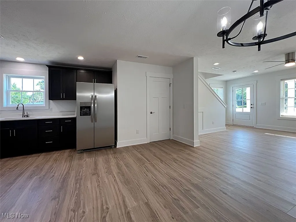 Kitchen, dining area and great room featuring stainless steel refrigerator with ice dispenser, dark cabinets, open floor plan, light countertops, and a textured ceiling