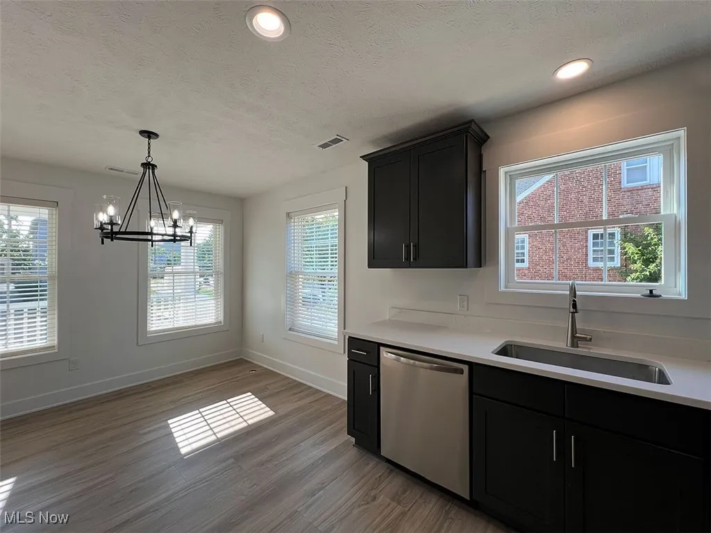 Kitchen and dining area with dishwasher, a chandelier, light wood-style flooring, white quartz countertops, and a textured ceiling