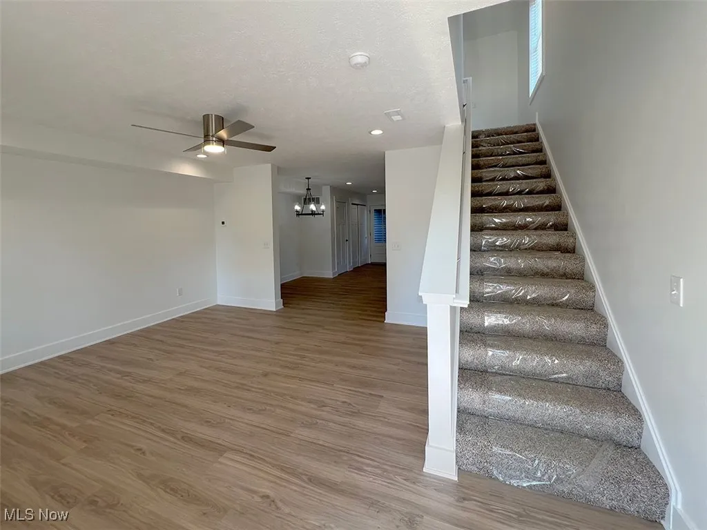 Great room with Staircase a ceiling fan, a chandelier, wood finished floors, and recessed lighting