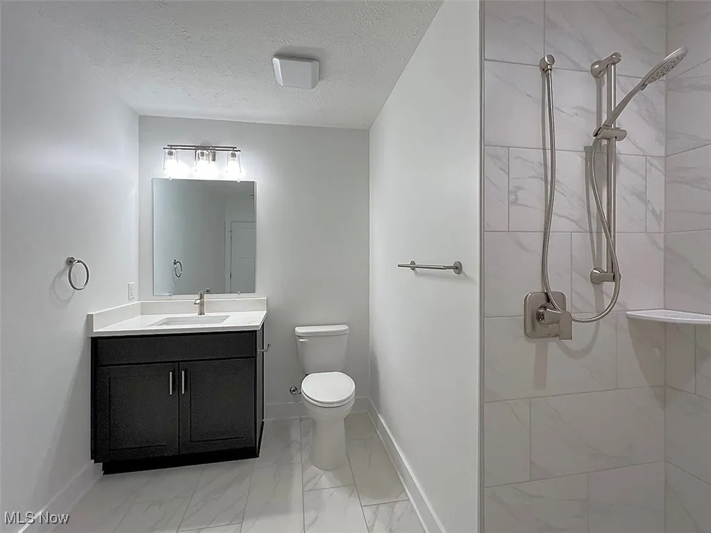 Master Bathroom featuring marble finish floors, vanity, tiled shower, and a textured ceiling