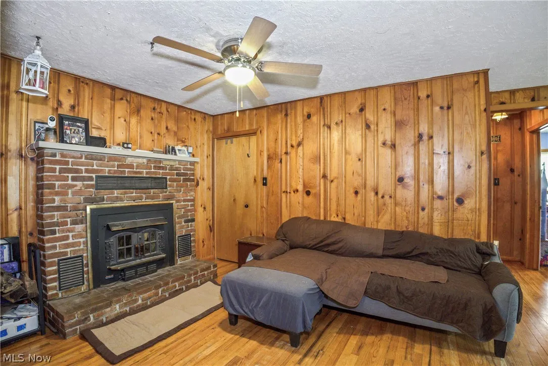 Living room featuring li / wood-style floors, a brick fireplace, ceiling fan, and wood walls