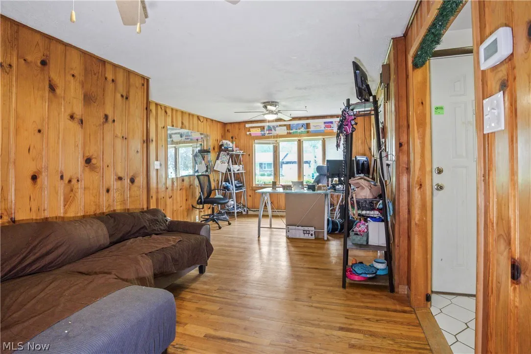 Living room with wooden walls, light hardwood / wood-style floors, and ceiling fan