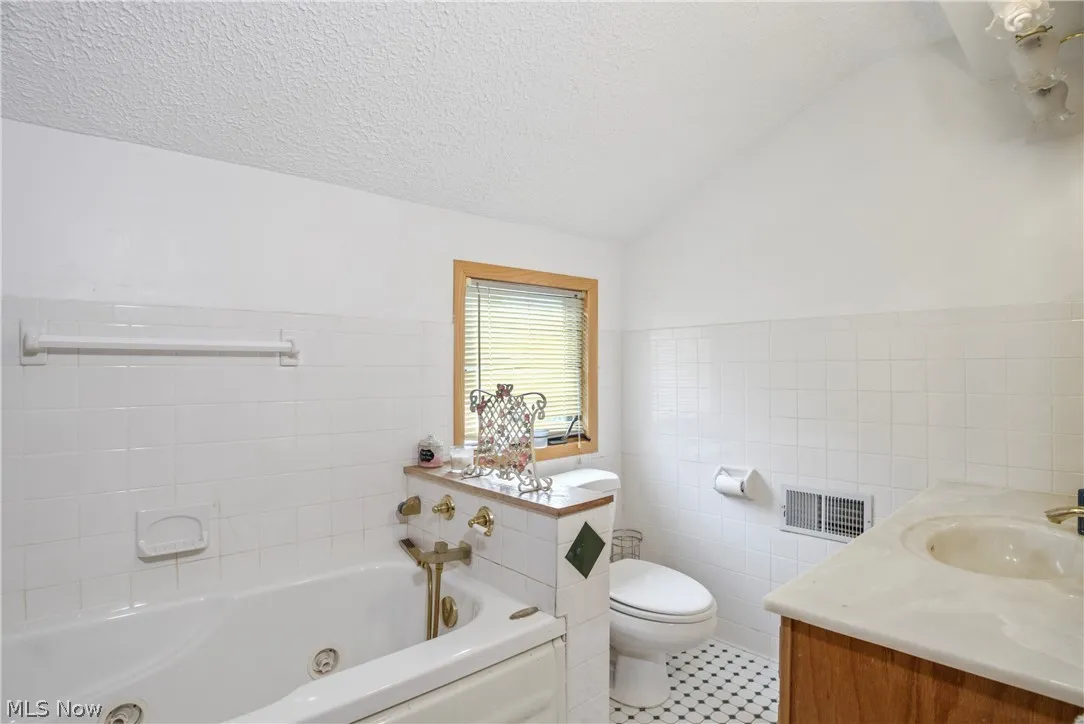 Bathroom featuring tile walls, toilet, lofted ceiling, a textured ceiling, and vanity
