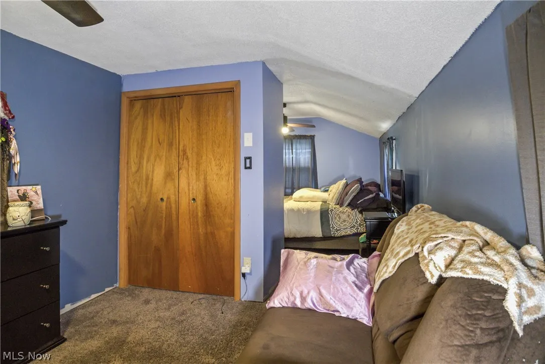 Bedroom featuring a closet, ceiling fan, carpet, a textured ceiling, and lofted ceiling