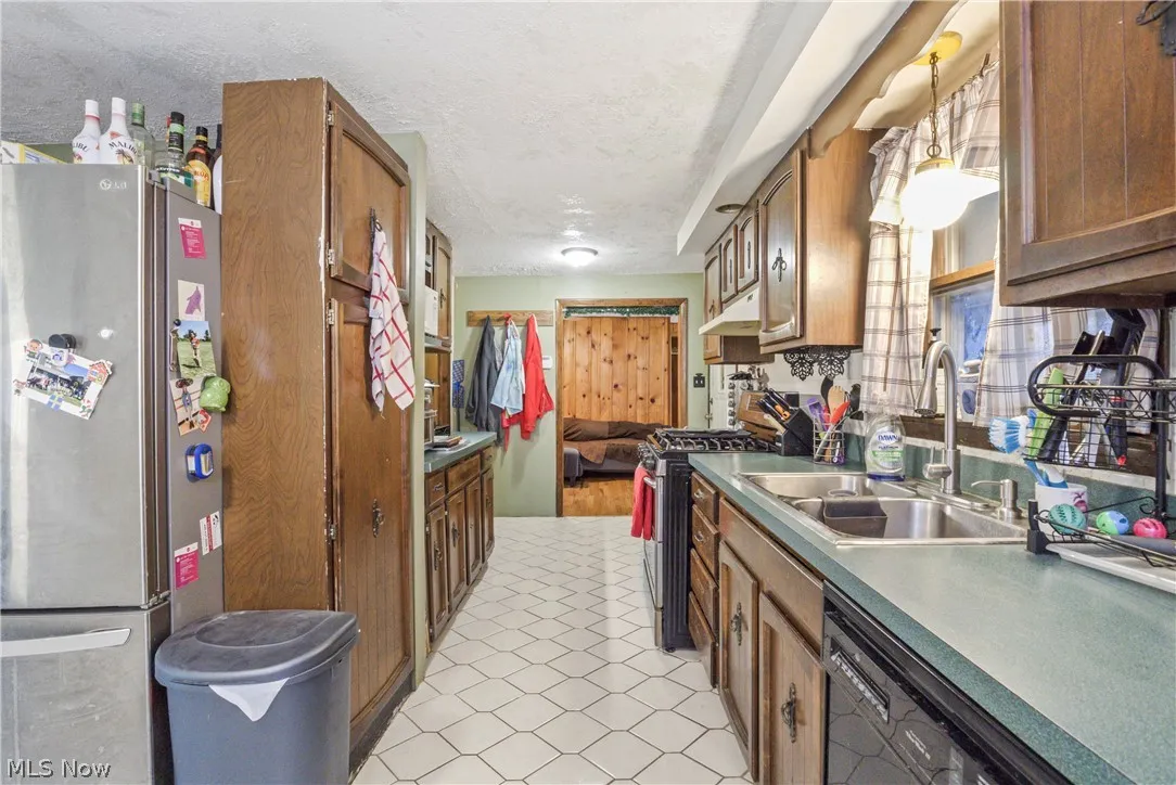 Kitchen with appliances with stainless steel finishes, a textured ceiling, sink, and decorative light fixtures