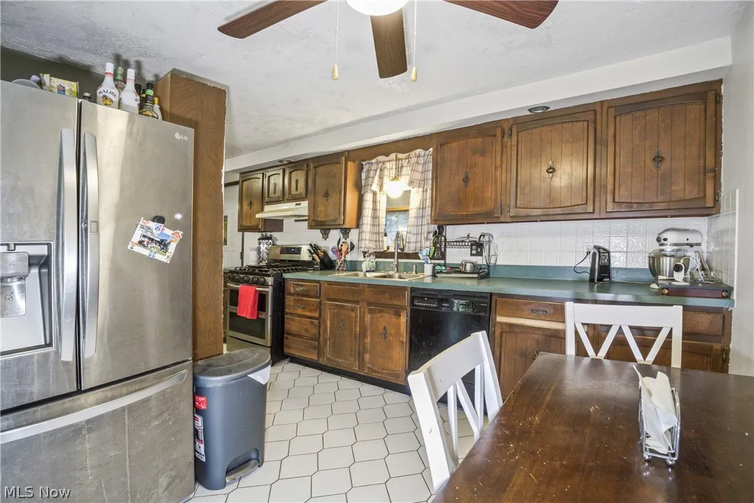 Kitchen with appliances with stainless steel finishes, ceiling fan, tasteful backsplash, sink, and light tile floors