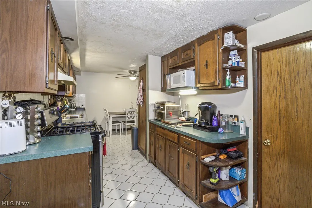 Kitchen with gas stove, ceiling fan, light tile flooring, and a textured ceiling