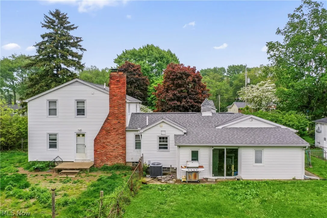 Back of property with central AC unit and a lawn