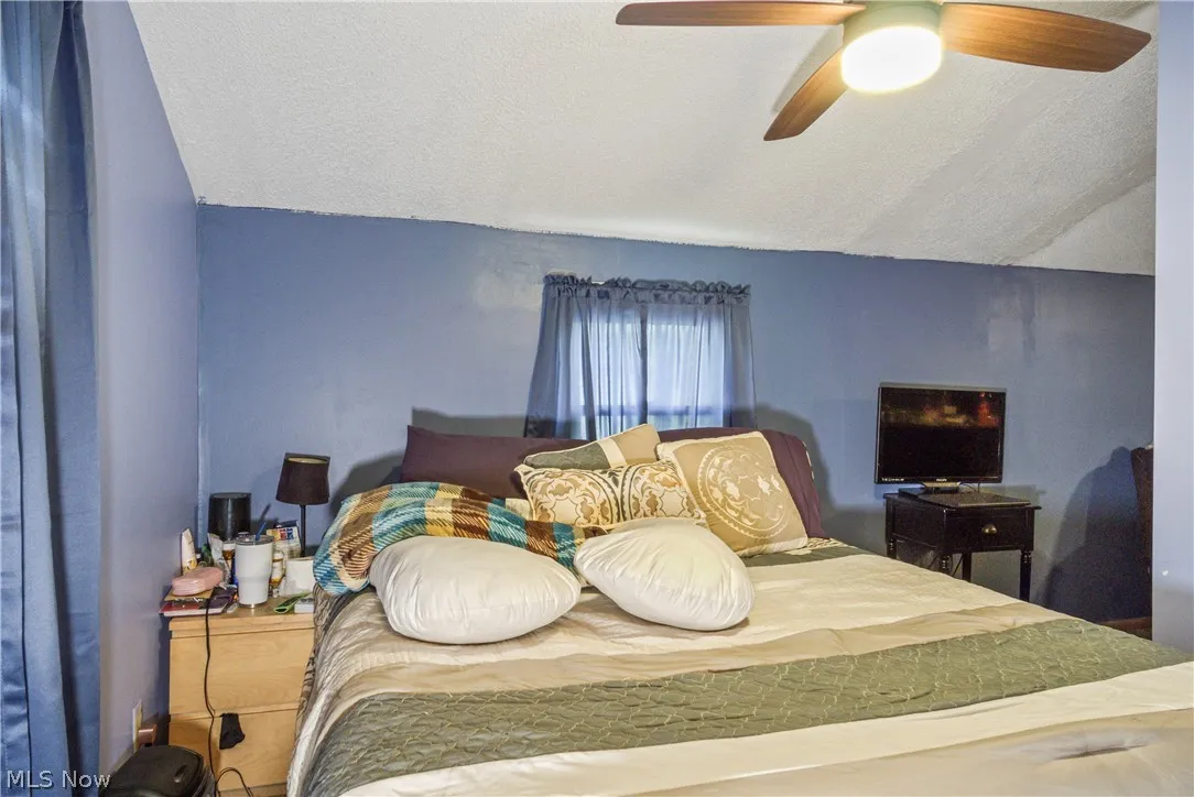 Bedroom featuring lofted ceiling, ceiling fan, and a textured ceiling