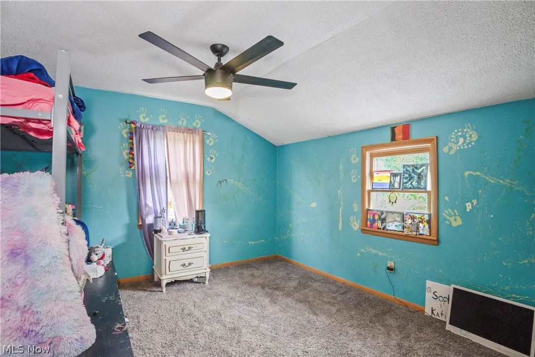 Bedroom with vaulted ceiling, carpet floors, ceiling fan, and a textured ceiling