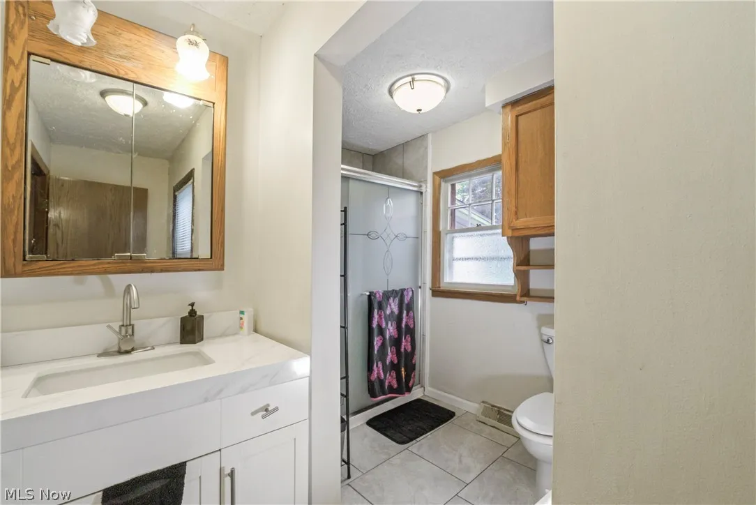 Bathroom with a textured ceiling, vanity, toilet, and tile flooring