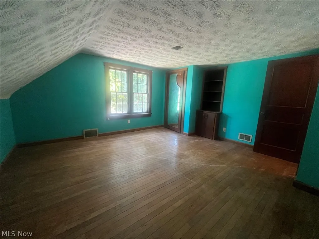 Unfurnished bedroom with a textured ceiling, dark hardwood / wood-style floors, and vaulted ceiling