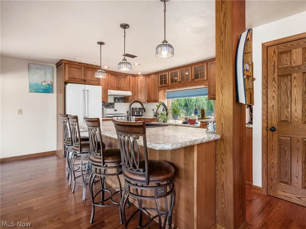 Kitchen with a kitchen breakfast bar, hanging light fixtures, range, light stone countertops, and dark wood-type flooring