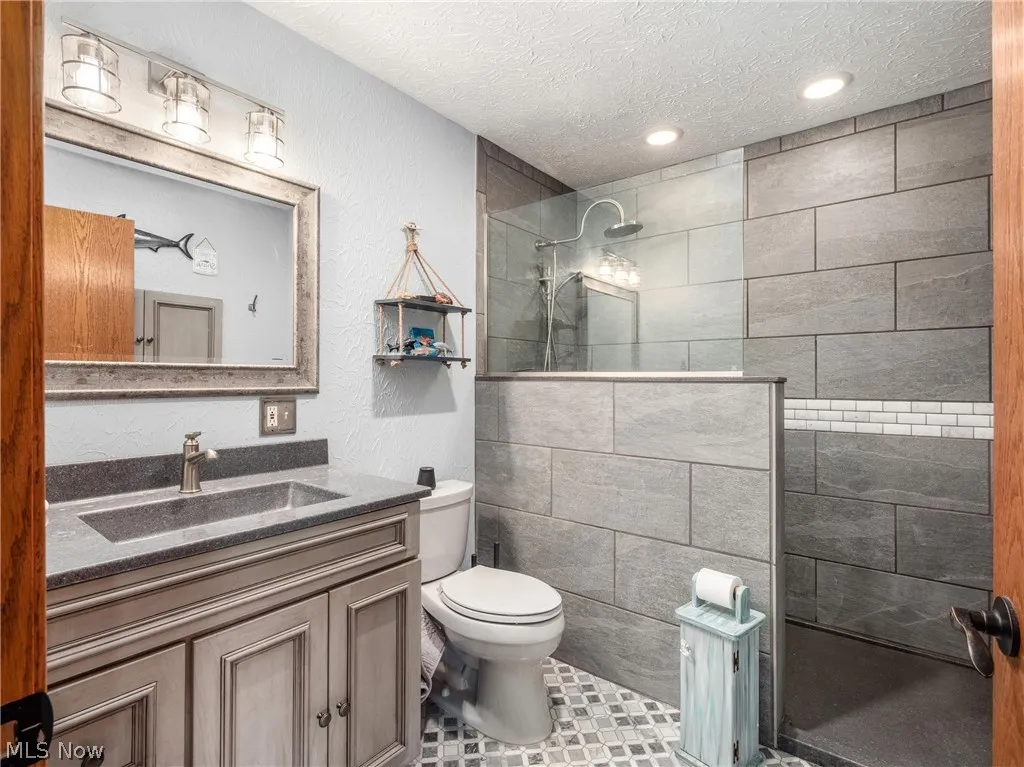 Bathroom with a shower with shower door, vanity, toilet, and a textured ceiling