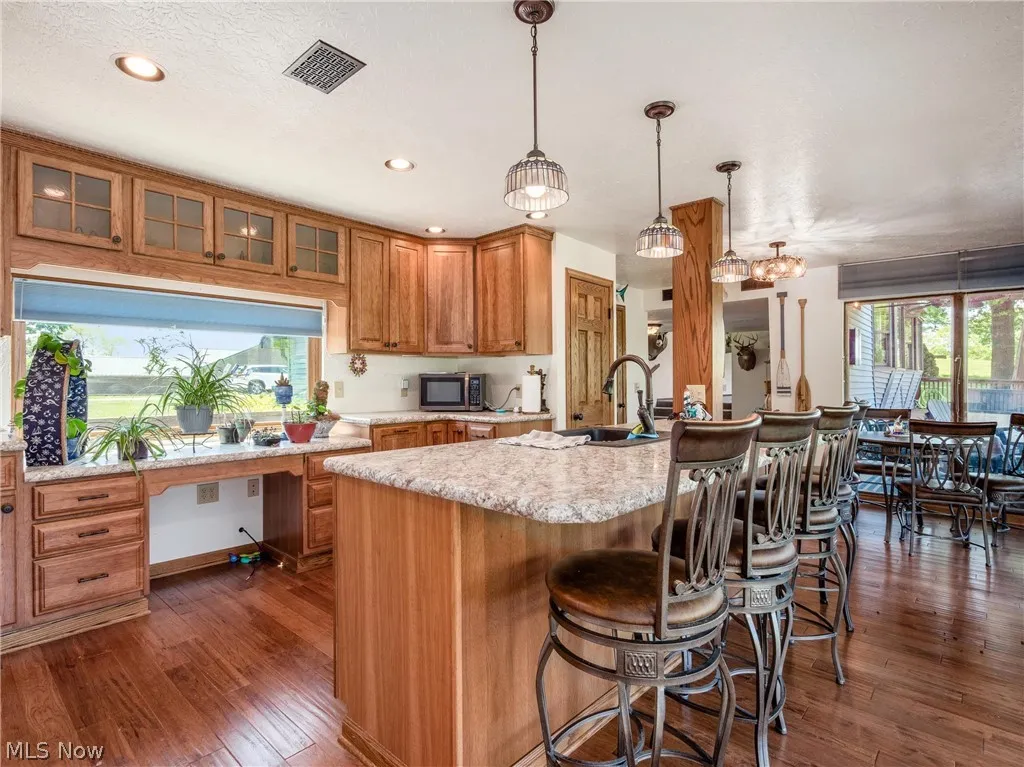 Kitchen with built in desk, pendant lighting, dark hardwood / wood-style flooring, sink, and a kitchen island with sink