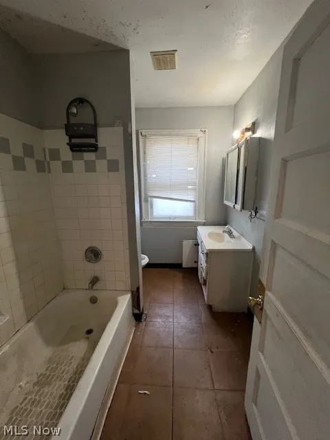 Full bathroom with tiled shower / bath combo, tile flooring, toilet, and vanity