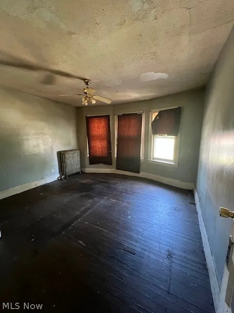 Unfurnished room with a textured ceiling, ceiling fan, hardwood / wood-style floors, and radiator heating unit