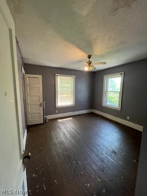Spare room with dark wood-type flooring, ceiling fan, and a textured ceiling