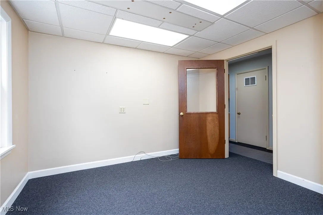 Empty room featuring a paneled ceiling and dark colored carpet