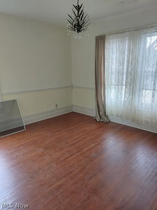 Unfurnished room with a wealth of natural light, an inviting chandelier, and hardwood / wood-style flooring