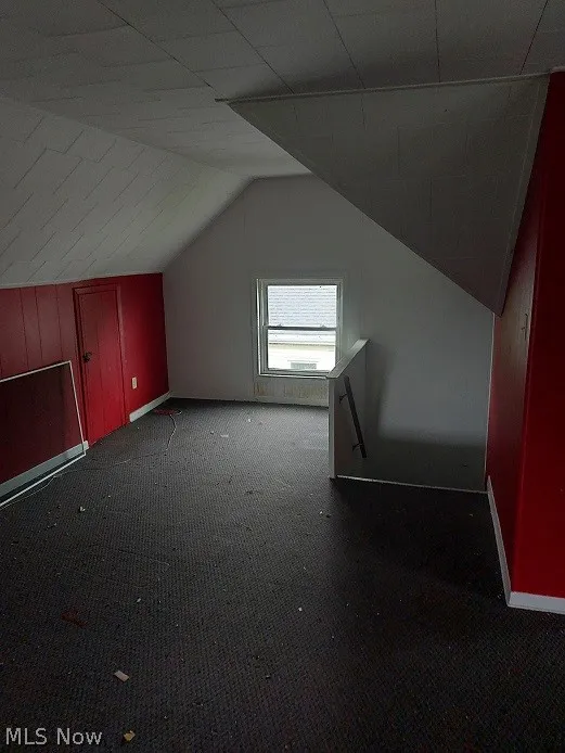 Additional living space featuring lofted ceiling and dark colored carpet