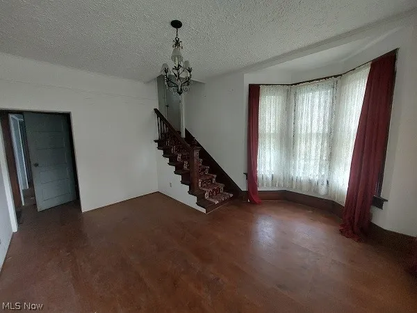 Unfurnished living room featuring a notable chandelier, a textured ceiling, and dark wood-type flooring