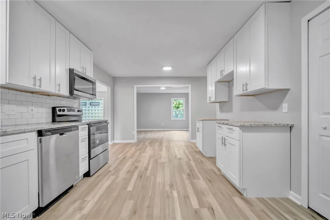 Kitchen with light stone counters, light laminate wood-style flooring, white cabinets, and appliances with stainless steel finishes