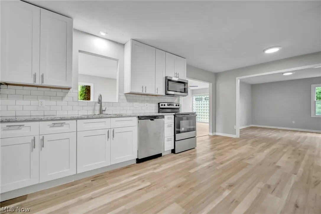 Kitchen featuring stainless steel appliances, white cabinets, light laminate wood-style floors, and backsplash