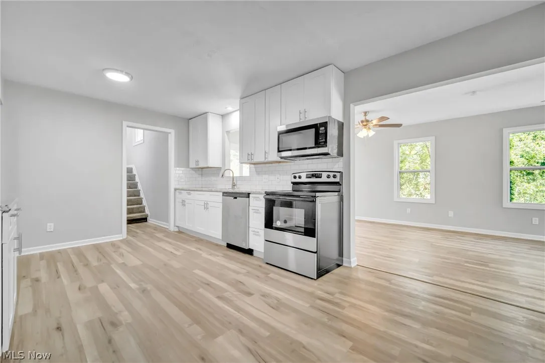 Kitchen with stainless steel appliances, white cabinetry, light  wood-style flooring, and backsplash