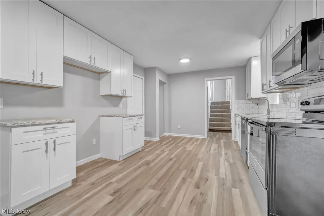 Kitchen with light laminate wood-style floors, tasteful backsplash, sink, white cabinetry, and appliances with stainless steel finishes
