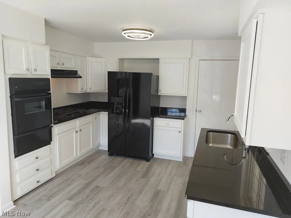 Kitchen with black appliances, white cabinetry, and light wood-type flooring
