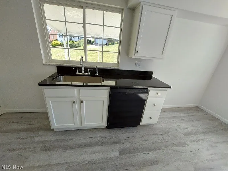 Kitchen featuring white cabinets, black dishwasher, sink, and light wood-type flooring