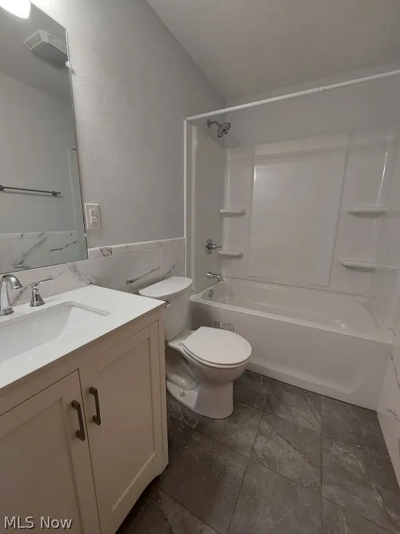 Full bathroom with tile flooring, vanity with extensive cabinet space, tile walls, toilet, and bathing tub / shower combination