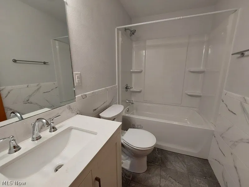 Full bathroom with tile flooring, shower / bathing tub combination, tile walls, backsplash, and toilet