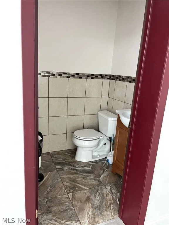 Bathroom featuring tile floors, tile walls, toilet, and vanity