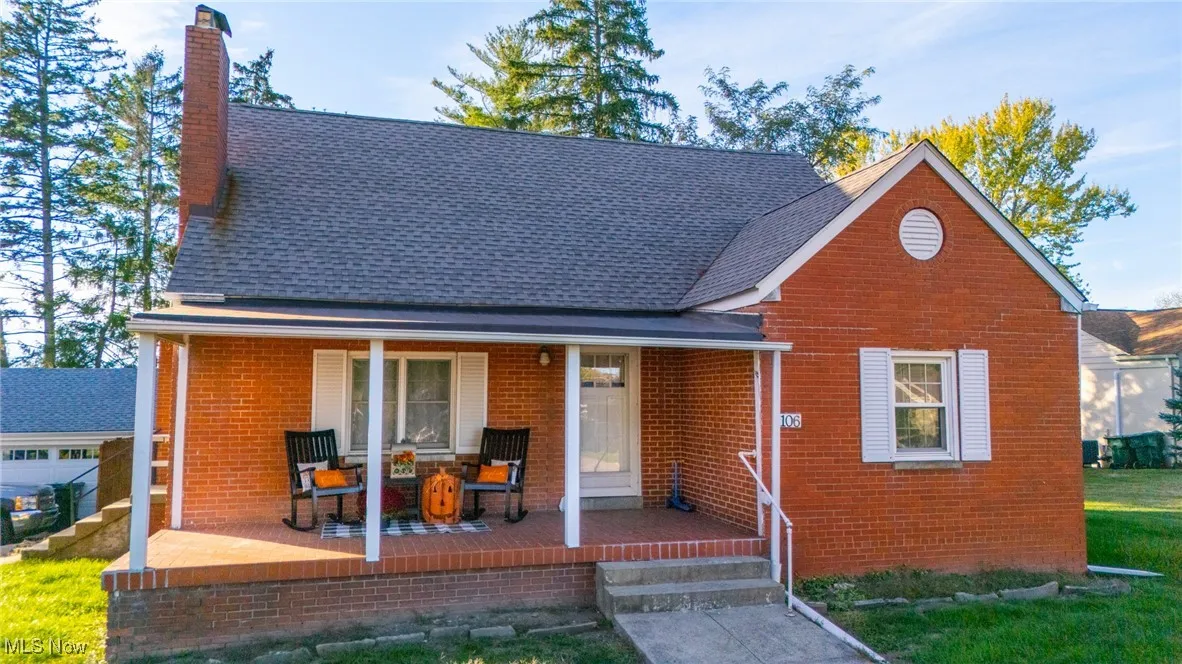 View of front facade featuring covered porch, a chimney, brick siding, roof with shingles, and a front lawn