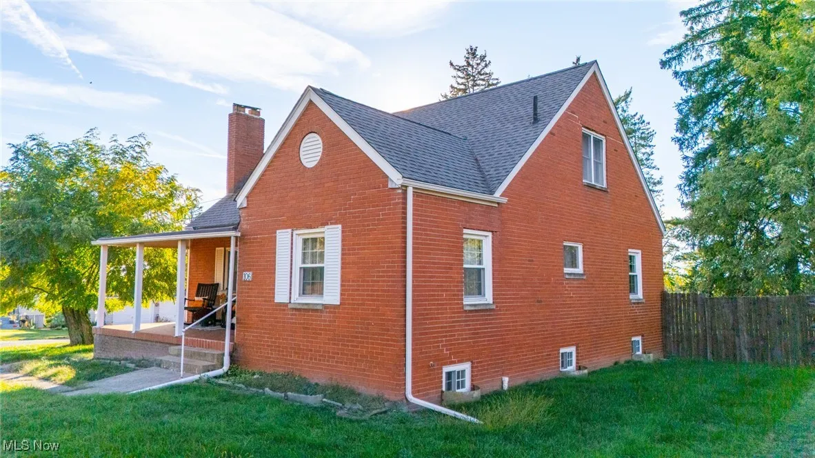 View of side of property featuring covered porch, a chimney, brick siding, and a shingled roof