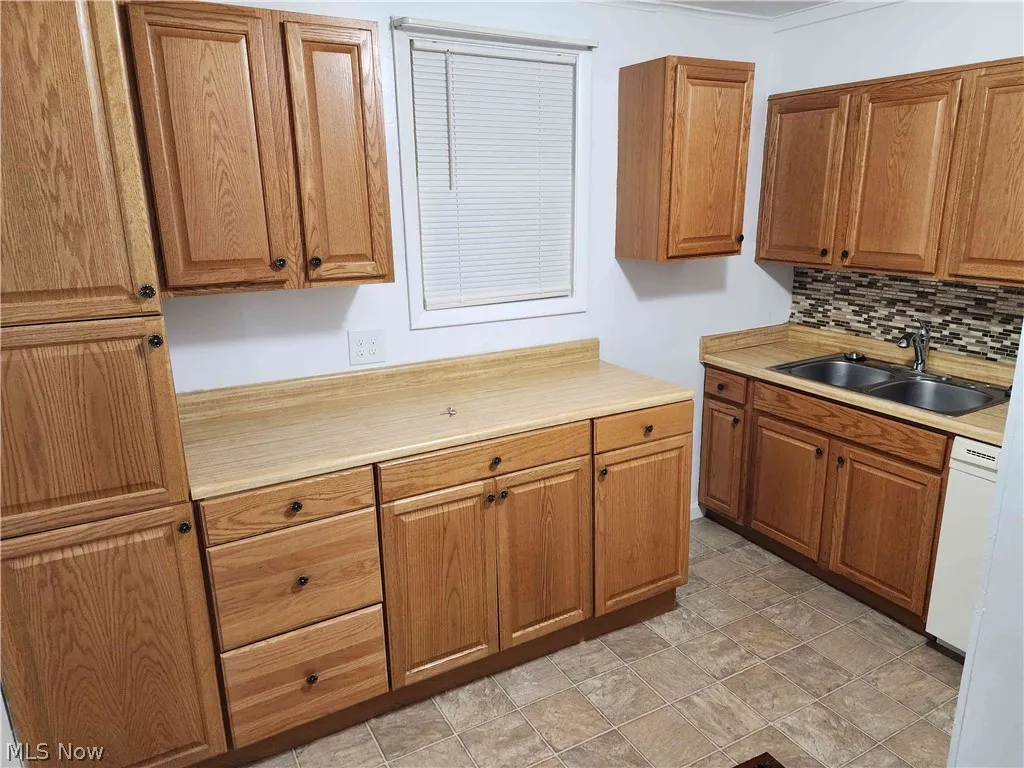 Kitchen with vinyl floors, white dishwasher, tasteful backsplash, and sink