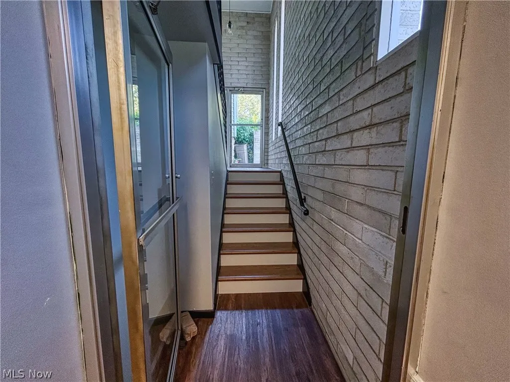 Entry/exit stairway featuring brick wall and dark hardwood / wood-style floors