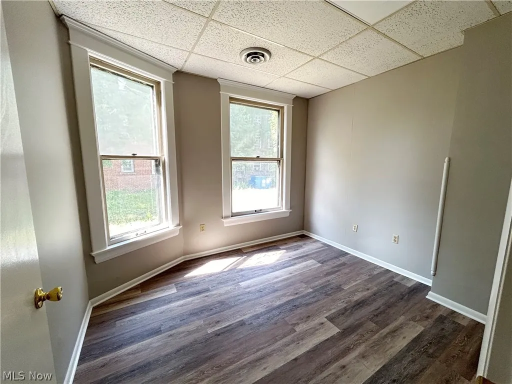 Unit A office with a drop ceiling, dark wood-style flooring, and windows