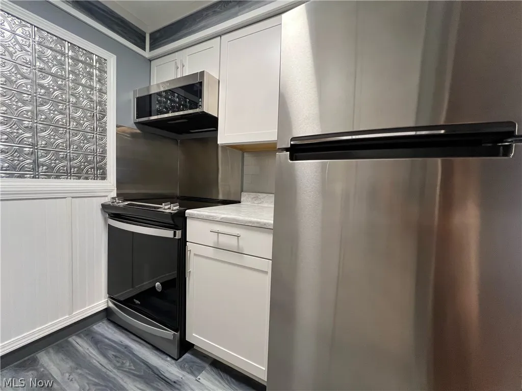 Kitchen featuring dark hardwood / wood-style floors, stainless steel appliances, crown molding, and white cabinets