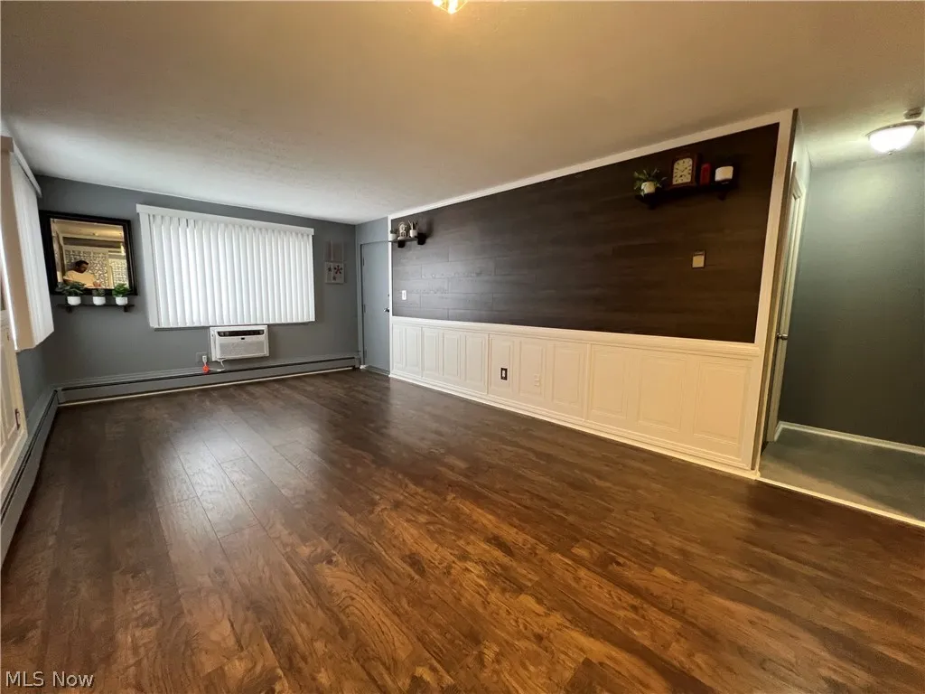Unfurnished room with dark wood-type flooring, baseboard heating, and a wall mounted air conditioner