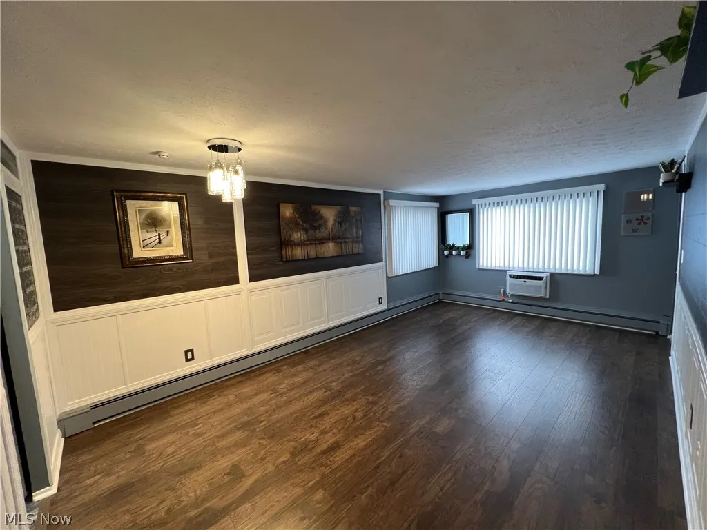 Unfurnished living room featuring dark hardwood / wood-style floors, a wall mounted air conditioner, a chandelier, and a textured ceiling