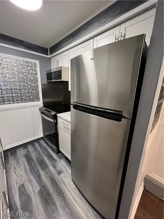 Kitchen with stove, stainless steel refrigerator, wood-type flooring, and white cabinets