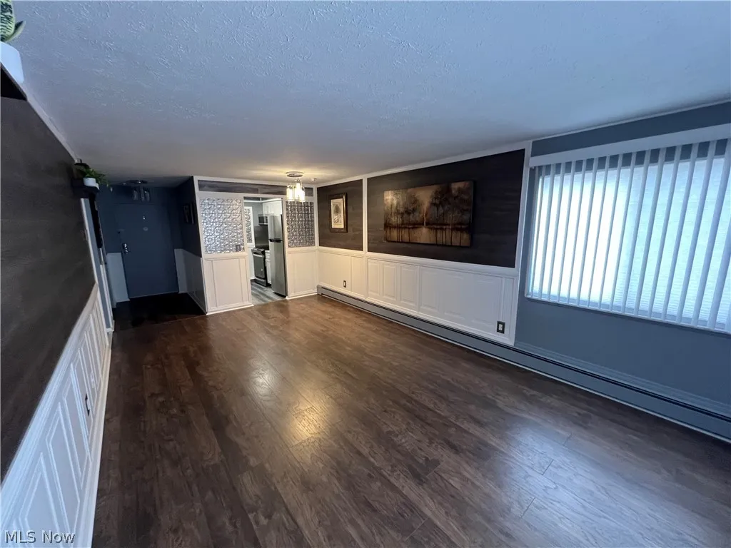 Unfurnished living room with a baseboard radiator, a textured ceiling, and dark hardwood / wood-style floors